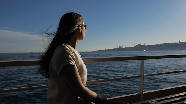 Mulher com cabelo ondulado viaja de navio apreciando a paisagem marítima