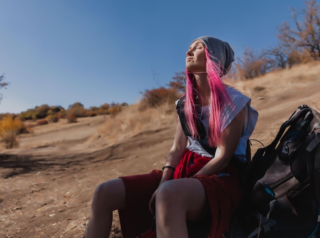 Mulher com cabelo rosa turista curtindo o sol sentada descansando no chão