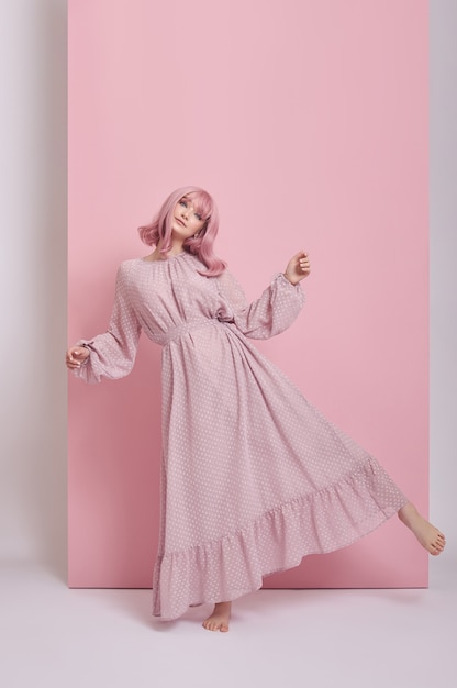 Mulher com cabelo tingido de rosa em um vestido longo. Retrato de uma menina com tintura de cabelo na parede rosa