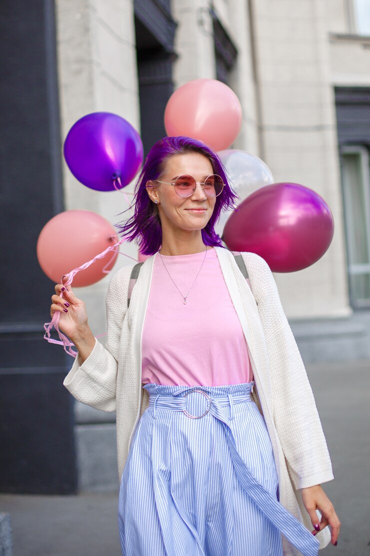Mulher com cabelo violeta em óculos cor de rosa, andando com airbaloons