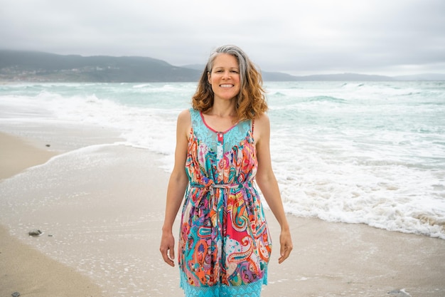 Mulher com cabelos grisalhos sorri para a câmera na praia