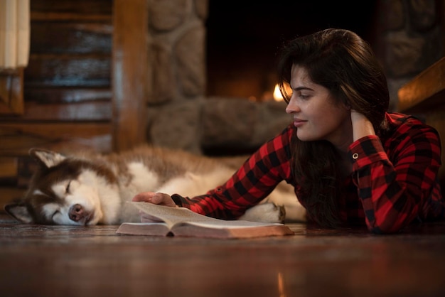 Mulher com cachorro husky siberiano sentado no chão de madeira em frente à lareira acesa