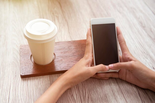 Mulher com café na mesa usando um telefone celular na cafeteria. Tela vazia para espaço de cópia