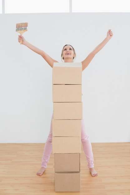 Foto mulher com caixas e pincel levantando as mãos na nova casa
