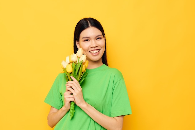 Mulher com camiseta verde de aparência asiática um buquê de flores amarelas fundo amarelo inalterado