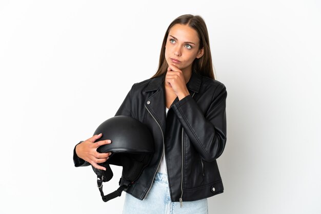 Mulher com capacete de motociclista sobre fundo branco isolado tendo dúvidas