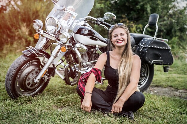 Mulher com capacete sentada na grama perto de uma motocicleta