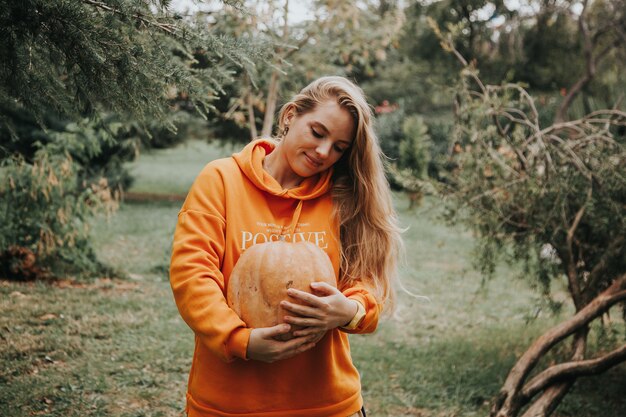 mulher com capuz laranja segurando uma abóbora laranja nas mãos no jardim. Conceito de outono