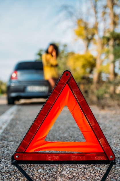 Foto mulher com carro quebrado e triângulo