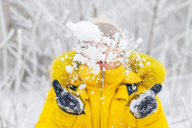 Mulher com casaco amarelo quente joga neve, divirta-se no fundo do inverno