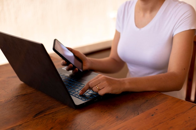 Mulher com celular na mão e digitando no laptop home office