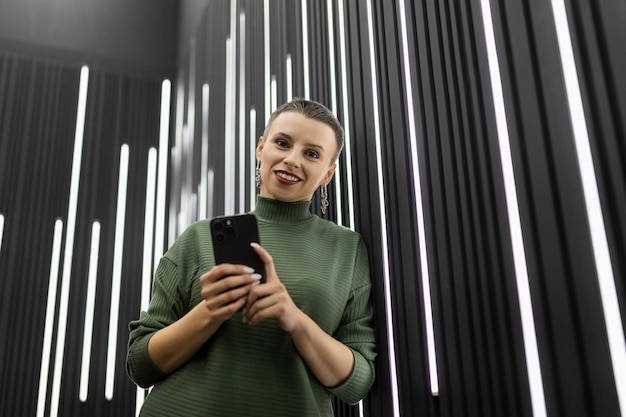 Mulher com celular perto de parede preta com lâmpadas led verticais
