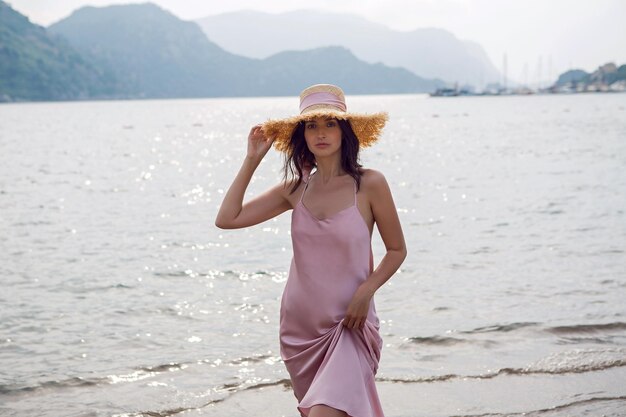 Foto mulher com chapéu de palha e vestido rosa caminhando na praia na turquia