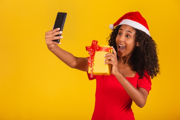 Mulher com chapéu de papai noel e tira selfie com caixa de presente