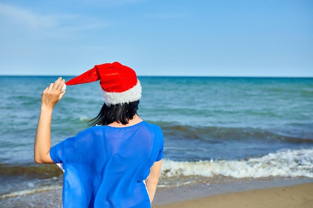 Mulher com chapéu de Papai Noel em pé na praia