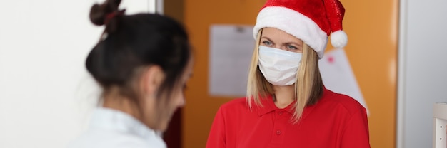 Mulher com chapéu de Papai Noel entrega caixa com presente para apartamento.