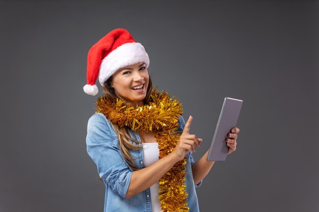 Mulher com chapéu de papai noel na cabeça usando tablet na véspera de natal.