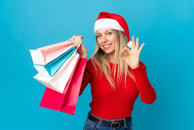 mulher com chapéu de Papai Noel segurando sacolas de compras