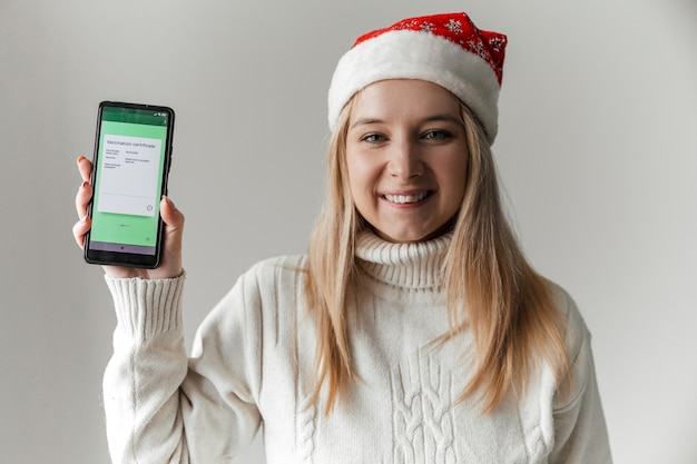 Mulher com chapéu de Papai Noel segurando smartphone com certificado eletrônico de vacinação cobiçado