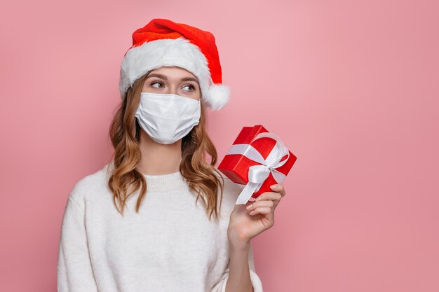 mulher com chapéu de Papai Noel sorrindo e segurando uma caixa de presente vermelha