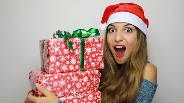 Mulher com chapéu de Papai Noel vermelho segurando uma pilha de presentes isolados