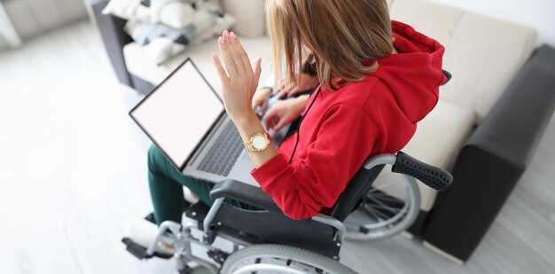 Mulher com deficiência em cadeira de rodas agitando a mão na tela do laptop