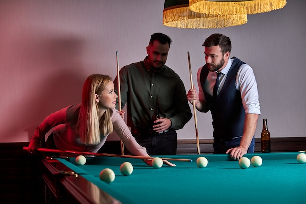 Mulher com dois amigos do sexo masculino joga bilhar no bar depois do trabalho, tem tempo de descanso e folga, preparando-se para jogar bolas de bilhar