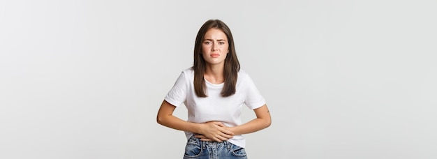 Mulher com dor de estômago se dobrando e segurando as mãos no desconforto da barriga de cólicas menstruais menina f