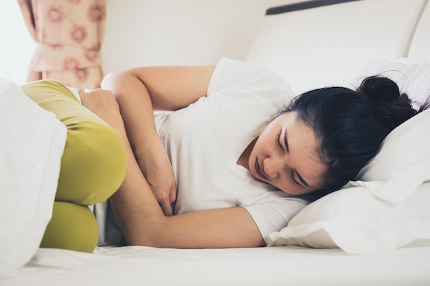 Mulher com dores de estômago a dormir na cama.