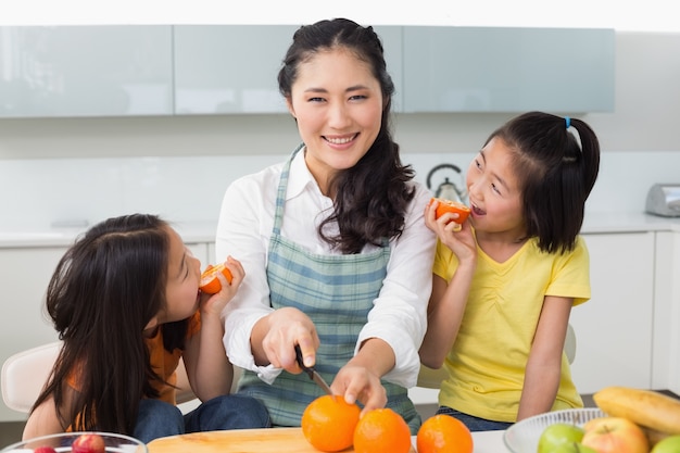 Mulher com duas filhas felizes cortando frutas na cozinha