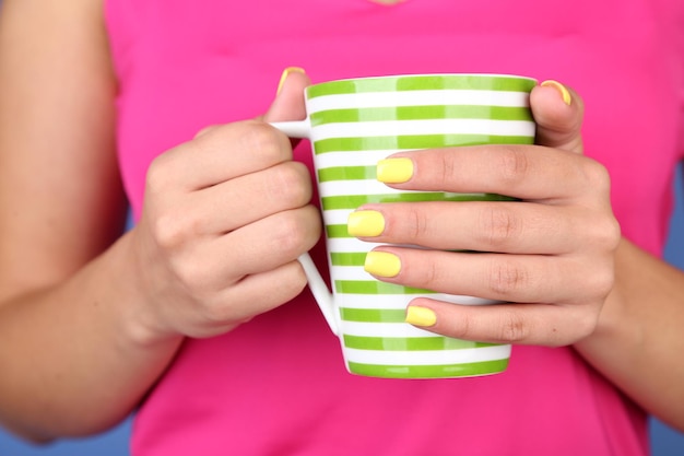 Mulher com elegantes unhas coloridas segurando caneca closeup na cor de fundo