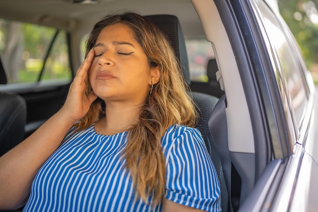 Foto mulher com enxaqueca sentada no carro com a mão na cabeça