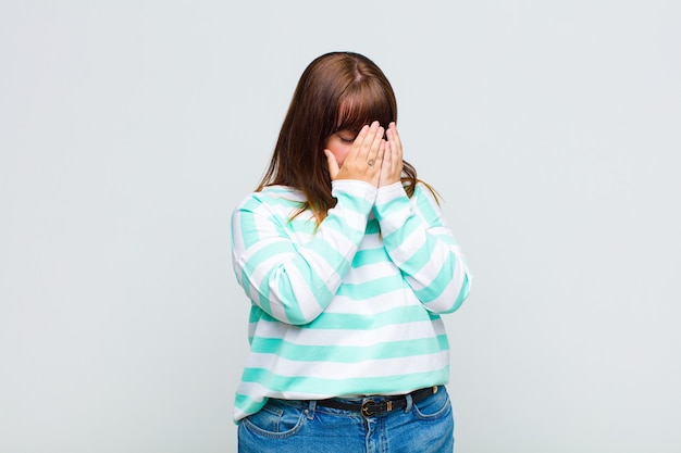 Mulher com excesso de peso cobrindo os olhos com as mãos com um olhar triste e frustrado de desespero, chorando, vista lateral