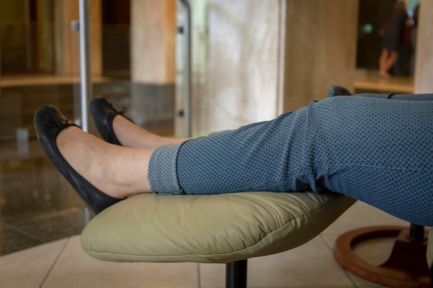 Mulher com excesso de peso com os pés para cima em sapatos casuais em um banquinho acolchoado em um close-up nas pernas