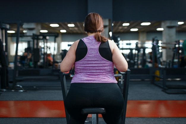 Mulher com excesso de peso fazendo exercícios na academia, vista traseira, treinamento ativo