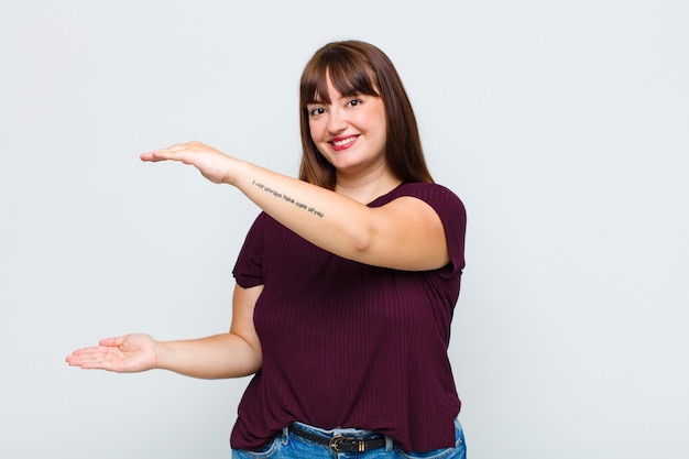 Mulher com excesso de peso sorrindo, sentindo-se feliz, positiva e satisfeita, segurando ou mostrando um objeto ou conceito no espaço da cópia