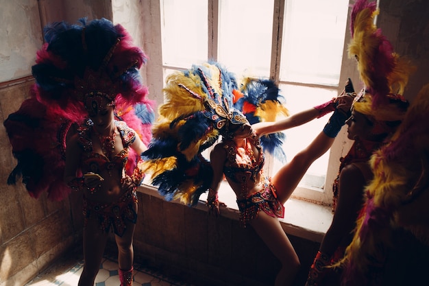 Foto mulher com fantasia de samba carnaval com plumagem de penas coloridas relaxando na entrada antiga com janela grande