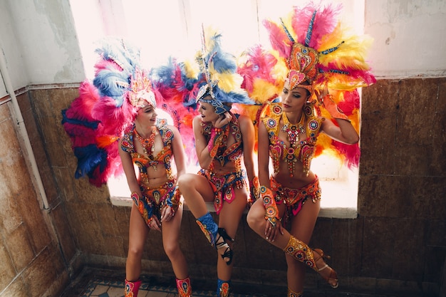 Mulher com fantasia de samba carnaval com plumagem de penas coloridas relaxando na entrada antiga com janela grande