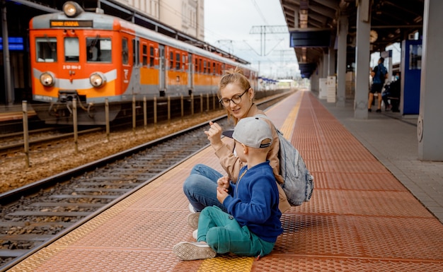 Mulher com filho na plataforma perto do trem. Menina com um menino pré-escolar sentado na estação de trem perto do trem. Viaje de trem. Mãe e filho esperando o trem. Viagem em família. Bydgoszcz.
