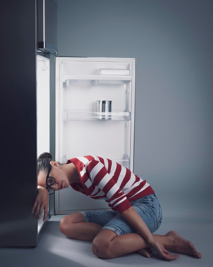 Foto mulher com fome apoiada no frigorífico vazio. ela tem fome, mas não tem comida em casa.