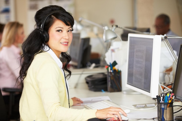 Mulher com fone de ouvido trabalhando na mesa no escritório criativo ocupado