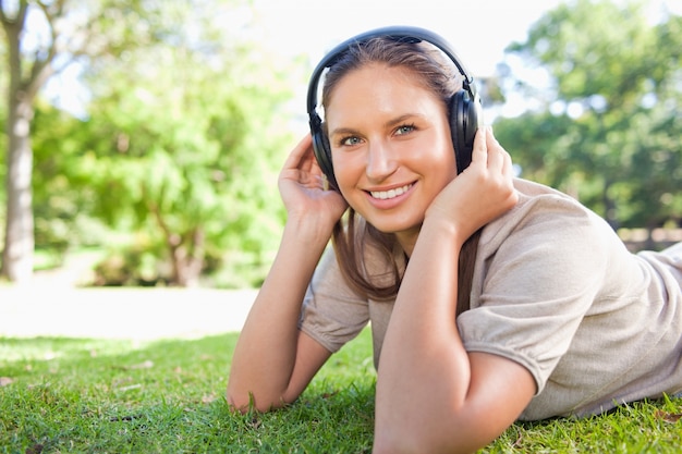 Mulher com fones de ouvido deitada no gramado