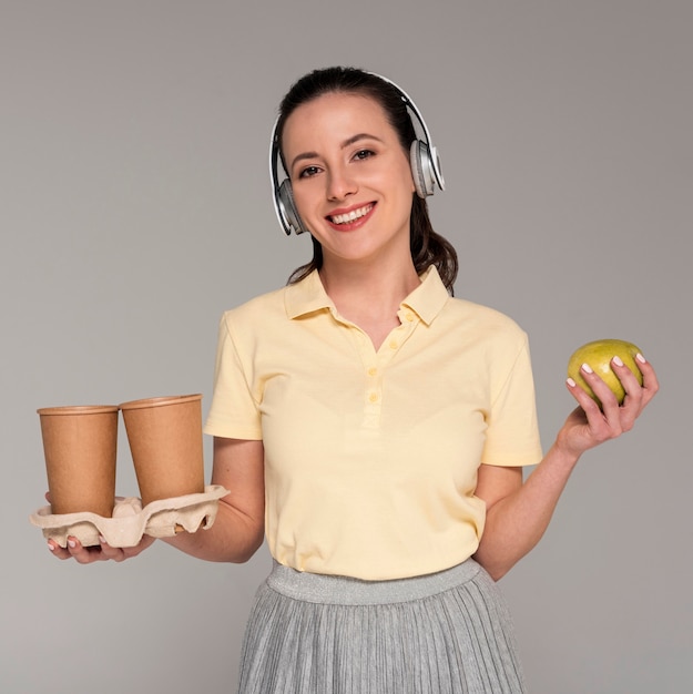 Foto mulher com fones de ouvido segurando copos de desenho animado e maçã