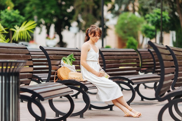 Mulher com garrafa de água reutilizável e bolsa de bambu, sacola de algodão com legumes no parque. Conceito de férias de verão