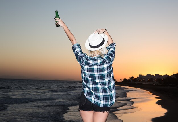 Mulher com garrafa de cerveja na beira-mar