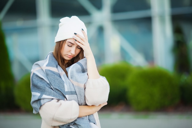 Mulher com gripe ao ar livre, vestindo um cachecol