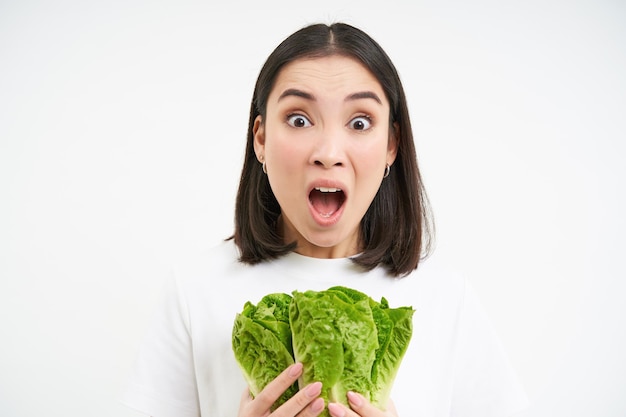 Mulher com gritos de cara chocada segura comida crua vegetal come repolho na dieta fundo branco