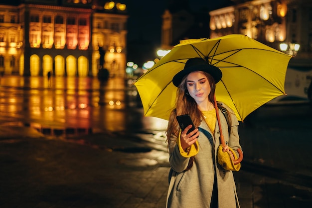 Mulher com guarda-chuva amarelo usando um smartphone no meio da noite