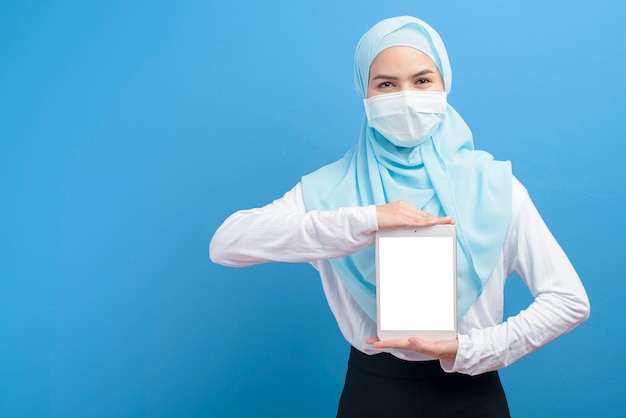 mulher com hijab usando máscara cirúrgica usando tablet