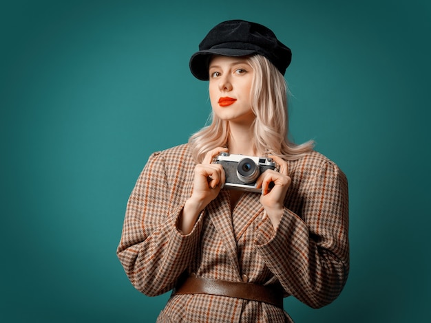 Mulher com jaqueta e boina estilo britânico com câmera vintage na parede verde